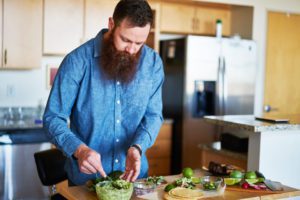 hipster guy with beard tasting homemade guacamole in kitchen
